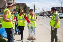 a team of young people wearing safety jackets pick up litter on a city street.
