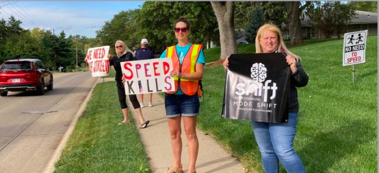 4 people on the sidewalk holding signs including: speed kills, mode shift omaha, & we need safe streets