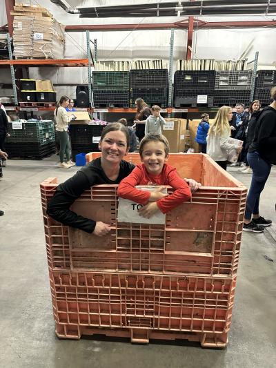 A mom and son, volunteer, in a donation bin at Open Door Mission, smiling while sorting toys